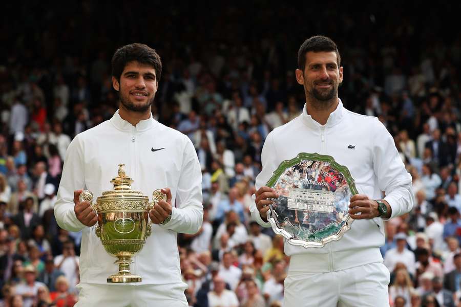 El español Carlos Alcaraz (izq.) sostiene el trofeo de ganador mientras posa con el serbio Novak Djokovic