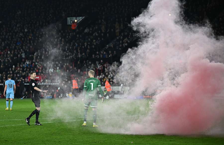 Referee Leigh Doughty talks with Sheffield United's Welsh goalkeeper Adam Davies as a flare goes off on the pitch