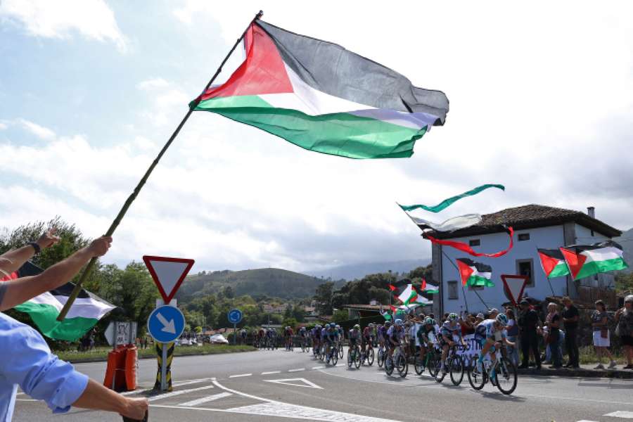 Riders pass protesters with Palestine flags during stage 13 