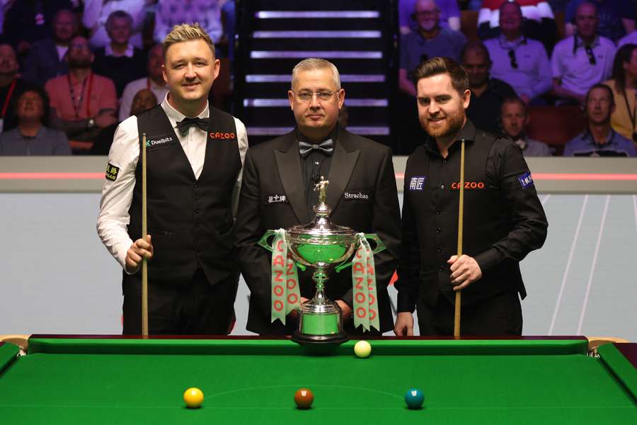 Kyren Wilson en Jak Jones poseren voor een foto met scheidsrechter Paul Collier en de Cazoo World Snooker Championship trofee