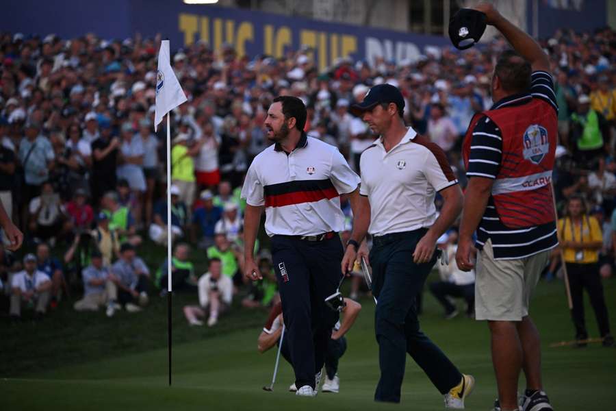 Rory McIlroy walks past Patrick Cantlay's caddy on the 18th green