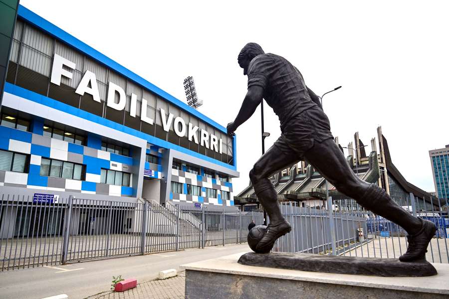 Fachada do estádio Fadil Vokrri, com a estátua lembrando o aracante e dirigente kosovar morto em 2018 Fachada do estádio Fadil Vokrri, com a estátua lembrando o aracante e dirigente kosovar morto em 2018