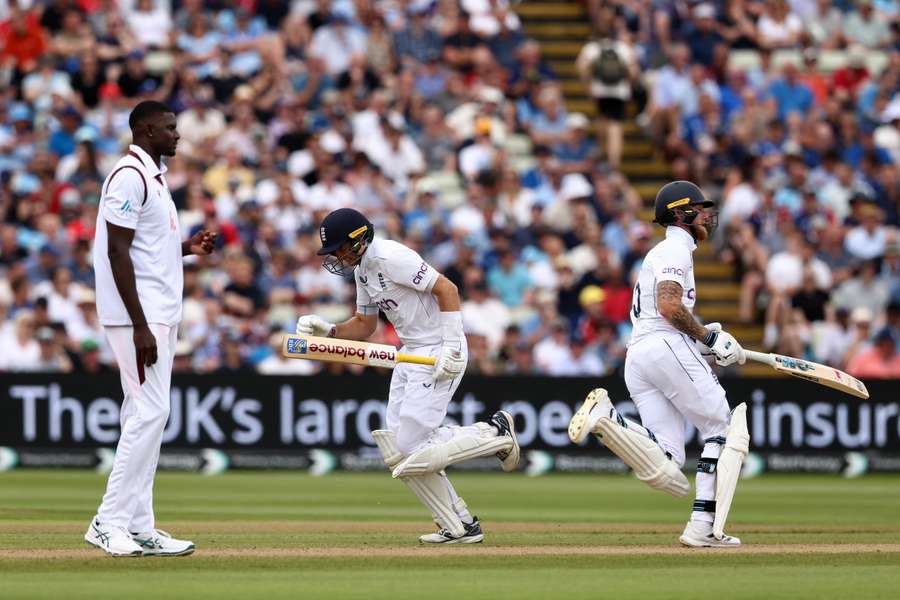 West Indies Jason Holder (L) watches as England's Joe Root (R) and England's captain Ben Stokes add runs