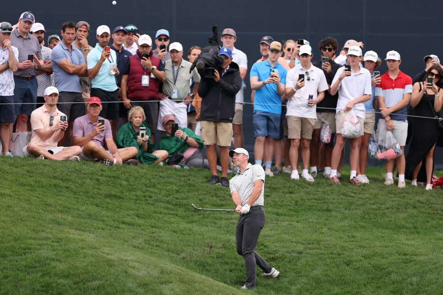 Rory McIlroy of Northern Ireland chips to the ninth green as fans look on 