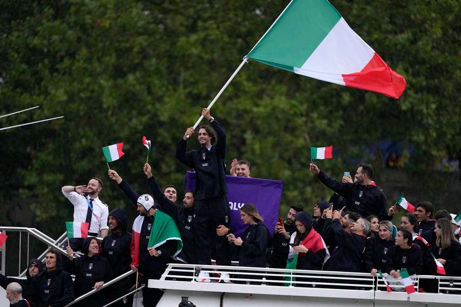 Gianmarco Tamberi waves an Italian flag as the Italian team parades along the Seine River in Paris