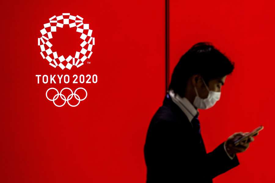 A man walking past a logo of the Tokyo 2020 Olympic Games