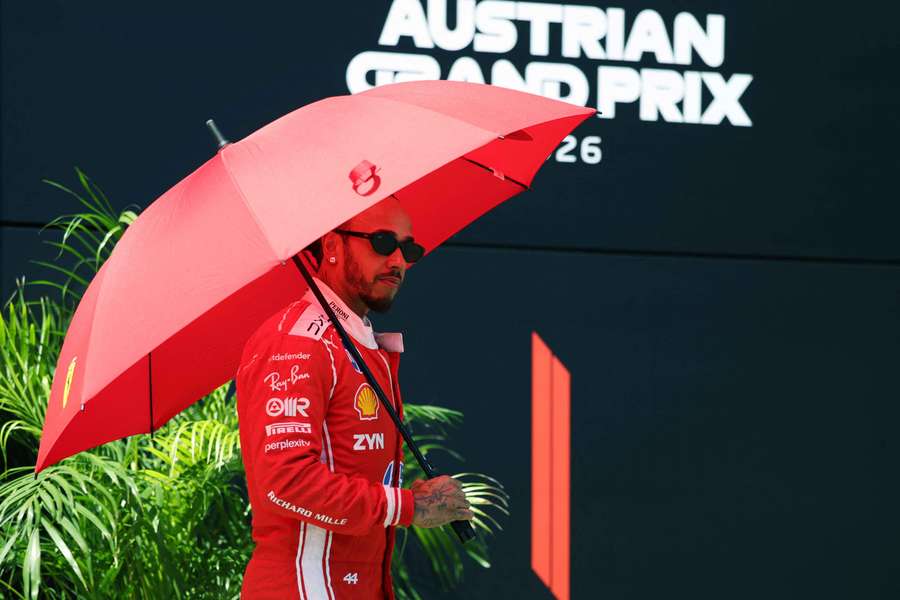 Lewis Hamilton takes cover under an umbrella amidst the heatwave ahead of the press conference