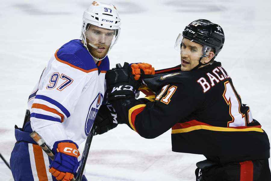 McDavid (97) holds the jersey of Flames forward Backlund