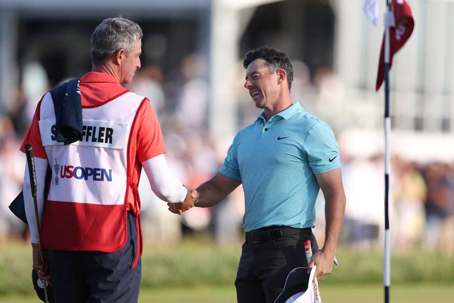 Rory McIlroy of Northern Ireland shakes hands with the caddie for Scottie Scheffler of the United States, Ted Scott on the 18th green