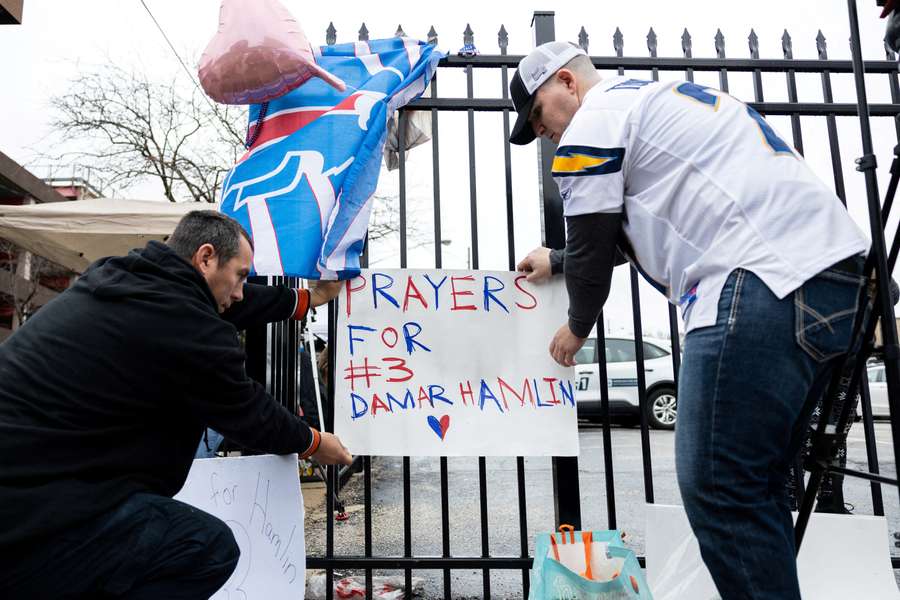 Football fans tape a sign to a fence during a vigil outside the University of Cincinnati Medical Center