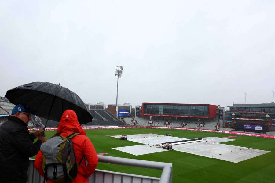 General view as spectators shelter under an umbrella as covers are on the pitch during a rain delay