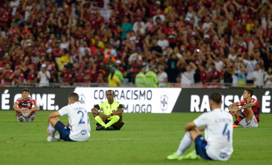 Referee Luiz Flavio de Oliveira sits amid Flamengo and Cruzeiro players during a tribute in support of Vinicius