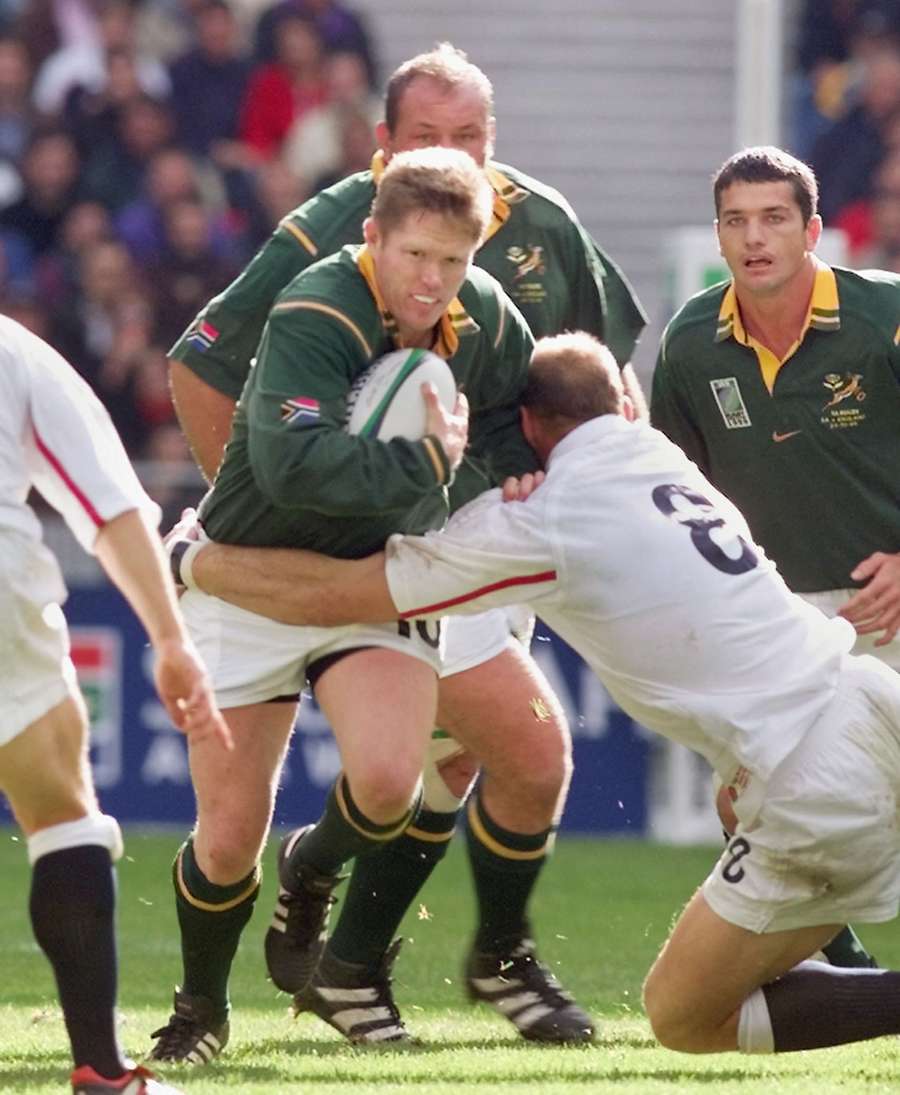 O defesa sul-africano Jannie de Beer tenta escapar à placagem do inglês Lawrence Dallaglio durante o jogo dos quartos de final do Campeonato do Mundo de Rugby entre a Inglaterra e a África do Sul no Stade de France em Saint-Denis, a norte de Paris, em 24 de outubro de 1999