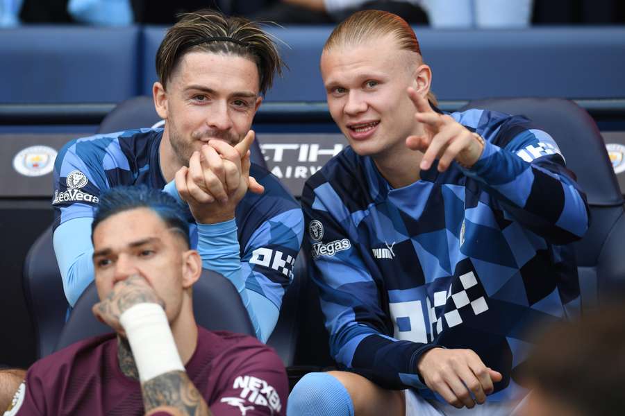 Manchester City's English midfielder Jack Grealish (L) talks with Manchester City's Norwegian striker Erling Haaland as they sit on the bench