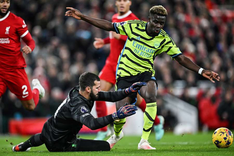 Alisson Becker attempts to stop the ball from Bukayo Saka