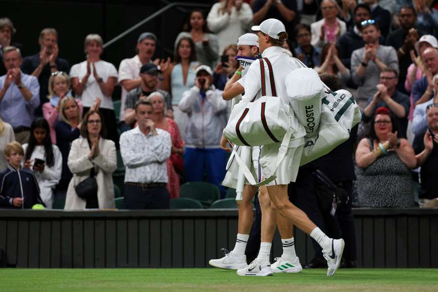 Bulgaria's Grigor Dimitrov (L) leaves the court flanked by Italy's Jannik Sinner after withdrawing following an injury