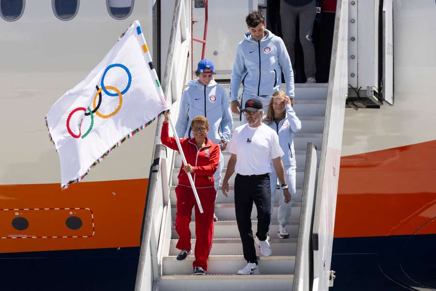 El alcalde Bass baja del avión con la bandera olímpica