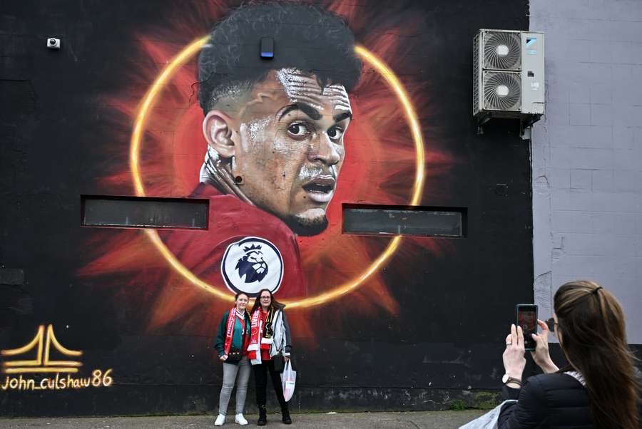 Liverpool fans pose with graffiti depicting Liverpool's Luis Diaz, by street artist John_Culshaw86
