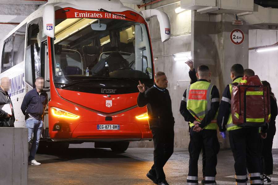 Firefighters stand next to Lyon's team bus, showing one window completely broken and another damaged