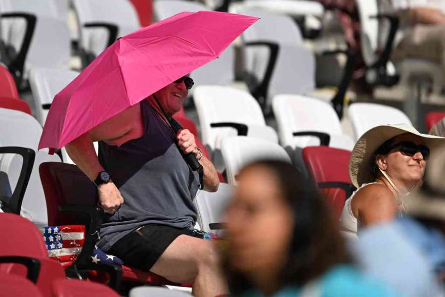 A spectator uses an umbrella to shield from the sun while watching athletes compete