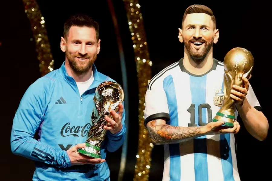 Messi en una foto con su estatua mientras sostiene la Copa del Mundo