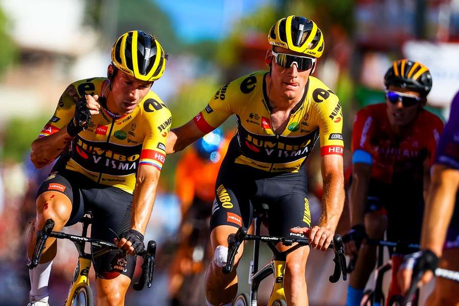 Roglic wordt door een ploeggenoot over de finish geholpen na een val in de Vuelta