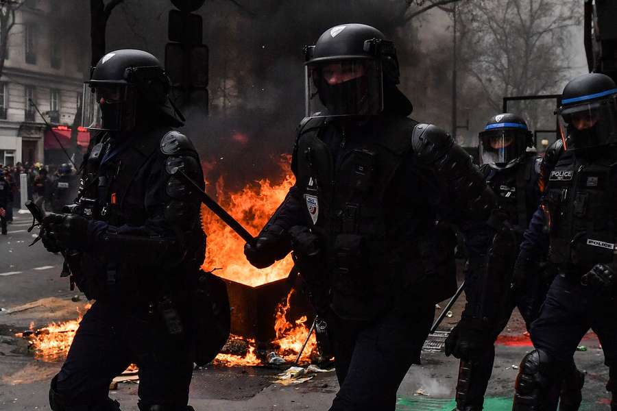 French riot police charge past burning garbage bins after riots earlier this year