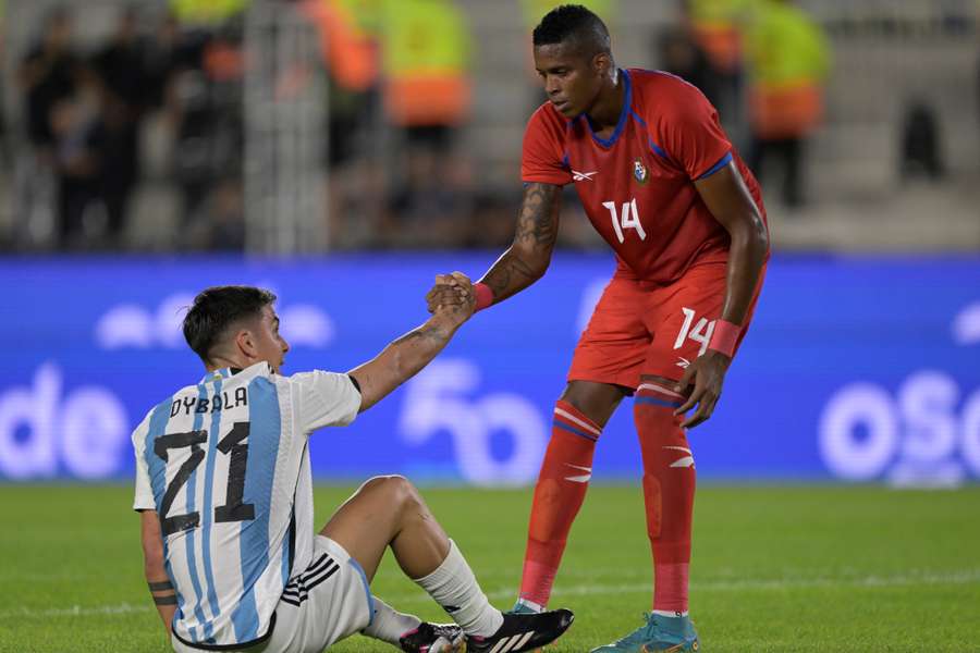 Gilberto Hernandez (R) helps Argentina forward Paulo Dybala stand up