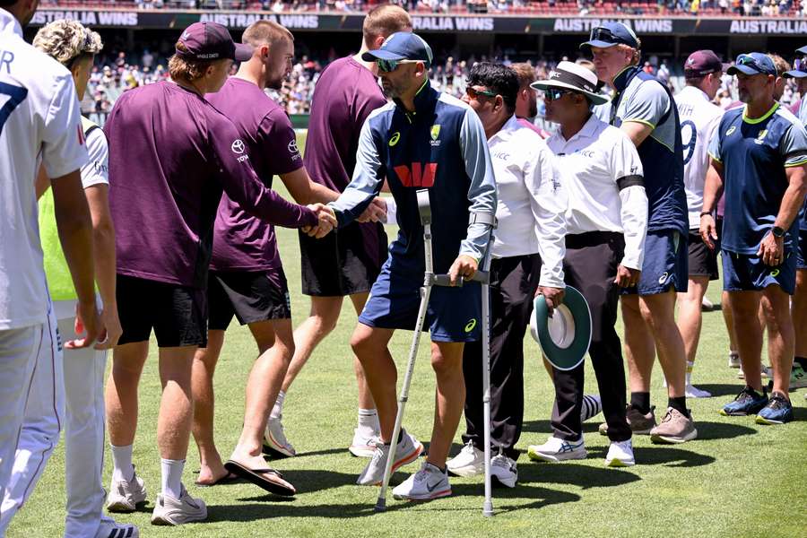 Nathan Lyon shakes hands with his English opponents whilst on crutches. 
