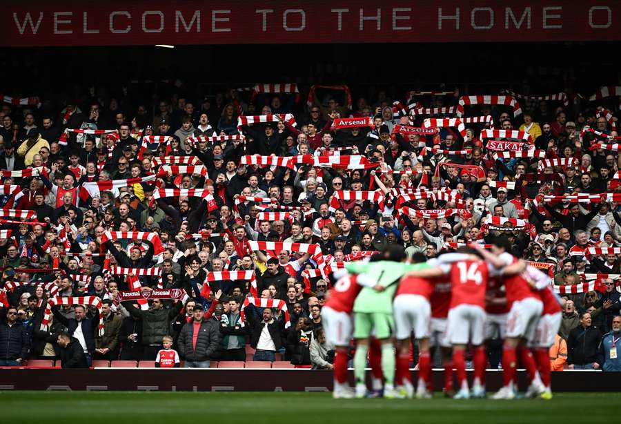 Arsenal fans holds scarves up inside the stadium as Arsenal players huddle before the match