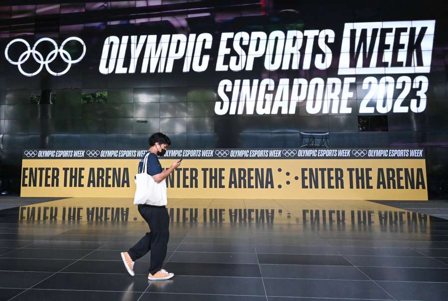 This photo taken on June 19, 2023 shows a man walking past a giant screen displaying a banner for the Olympic Esports week at Suntec City convention and exhibition hall in Singapore