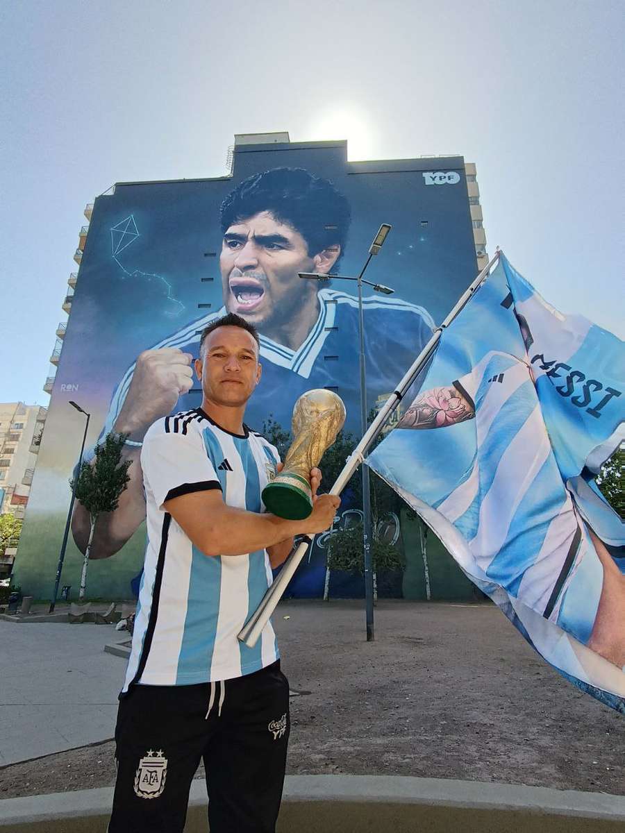 Ein Fan mit Argentinien-Flagge vor einem Haus mit Graffiti-Bemalung Maradonas