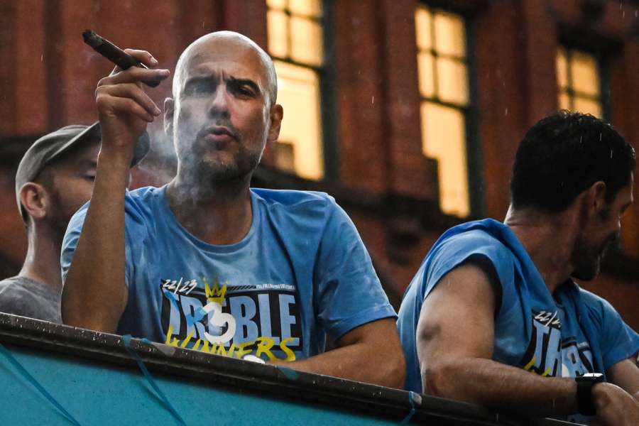 El entrenador del Manchester City, Pep Guardiola, fuma un puro mientras celebra la victoria con sus jugadores en un desfile en autobús descubierto.