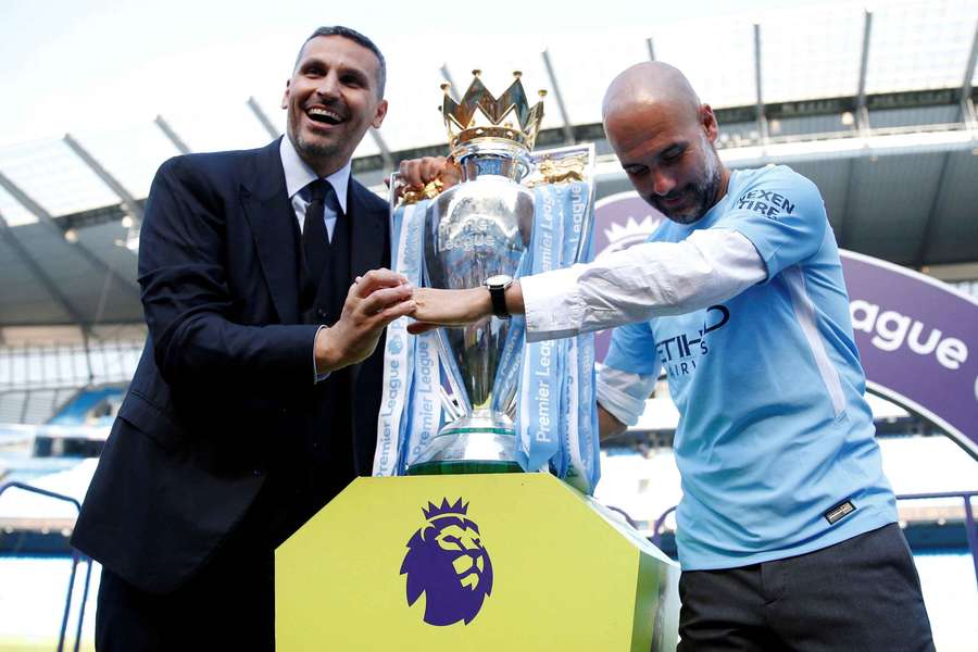 Guardiola (dir.) com o CEO do City e uma taça da Premier League que pode ser retirada da sala de troféus