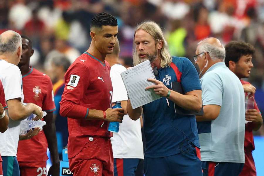 Austin MacPhee (dir.) dá indicações a Cristiano Ronaldo (esq.) durante o Mundial-2026 Austin MacPhee (dir.) dá indicações a Cristiano Ronaldo (esq.) durante o Mundial-2026