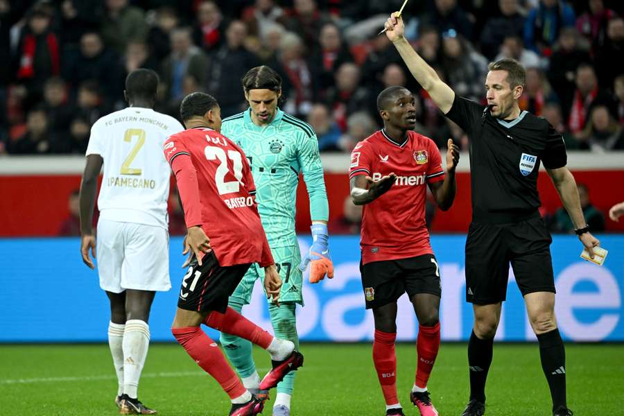 Arbitrul Tobias Stieler  îi arată cartonașul galben atacantului francez al echipei Leverkusen, Amine Adli 