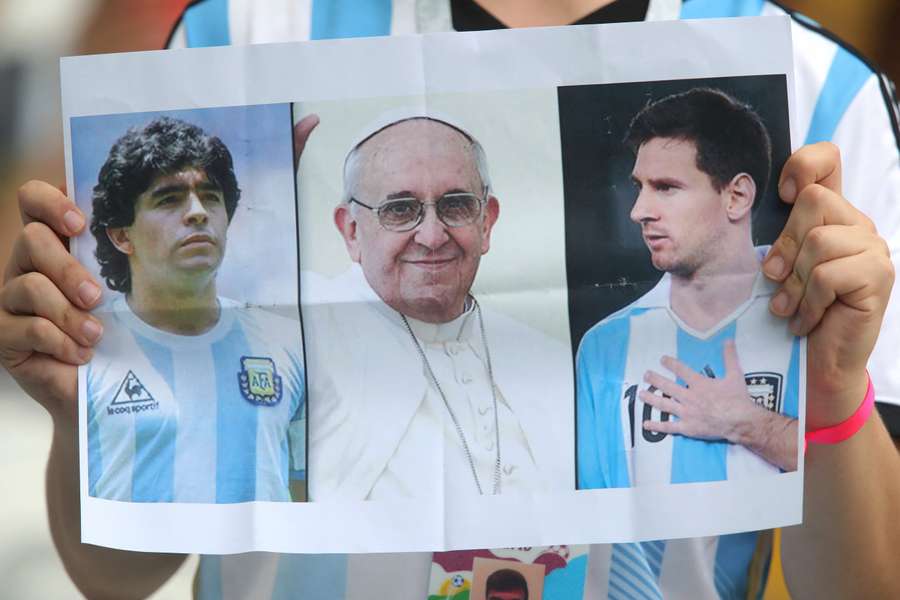 Un suporter argentinian ține un afiș cu Maradona, Papa Francisc și Lionel Messi