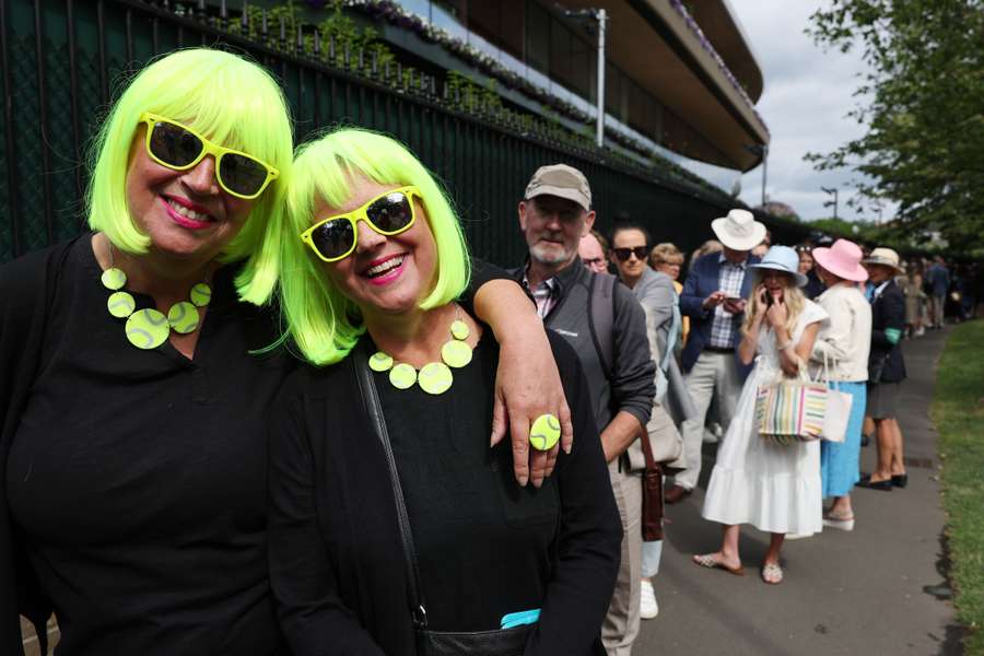 Two women sporting wigs pose as they queue to enter Wimbledon