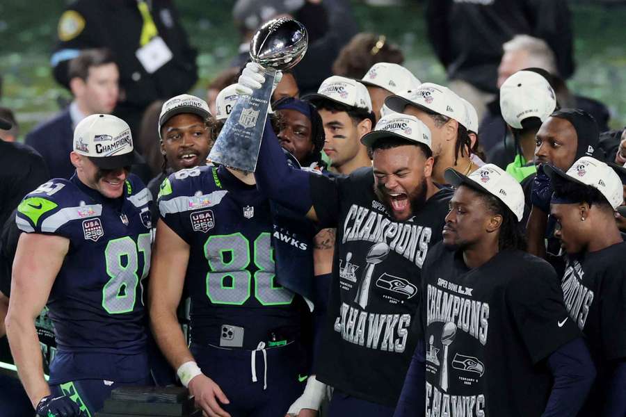 Seattle Seahawks players celebrate with the trophy on the podium after winning Super Bowl LX