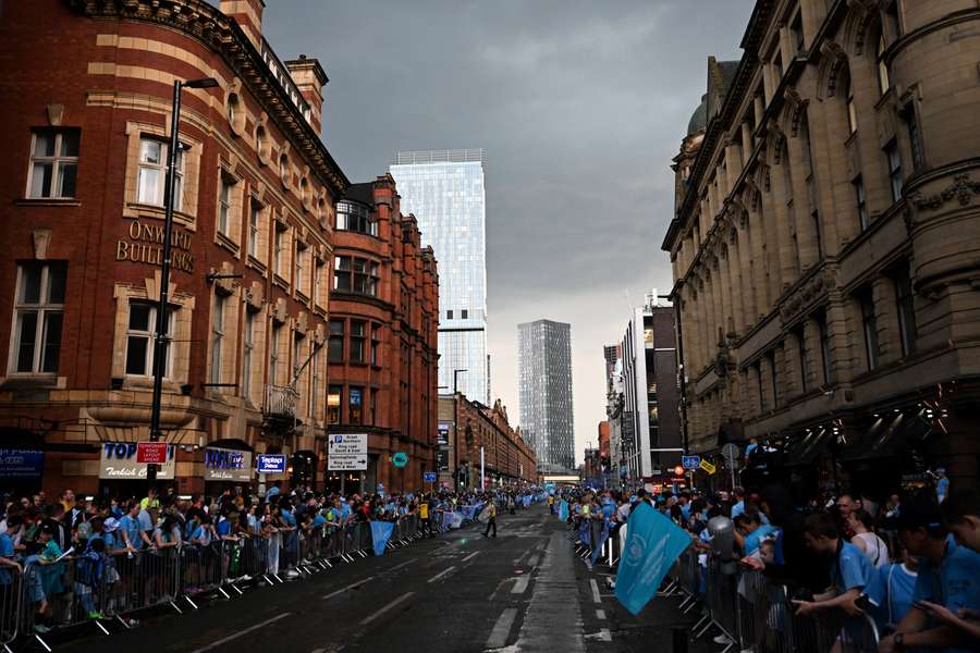 Manchester City's supporters celebrate and take shelter from the rain as they wait for the arrival of the players for an open-top bus victory parade