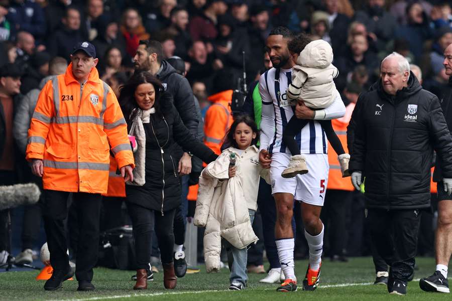 West Bromwich Albion's English defender #05 Kyle Bartley helps take members of his family away from an area of the ground where trouble has broken out