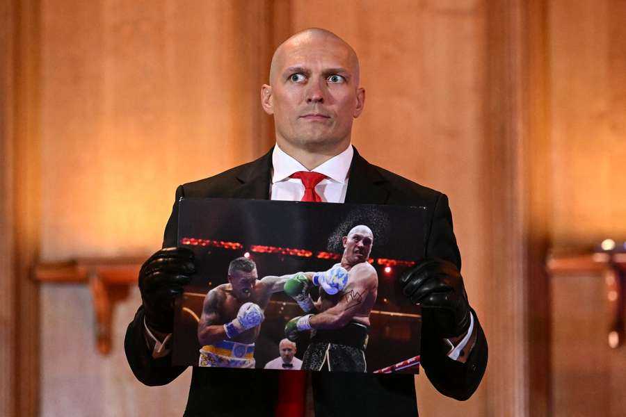 Oleksandr Usyk holds a photograph signed by Tyson Fury during the press conference