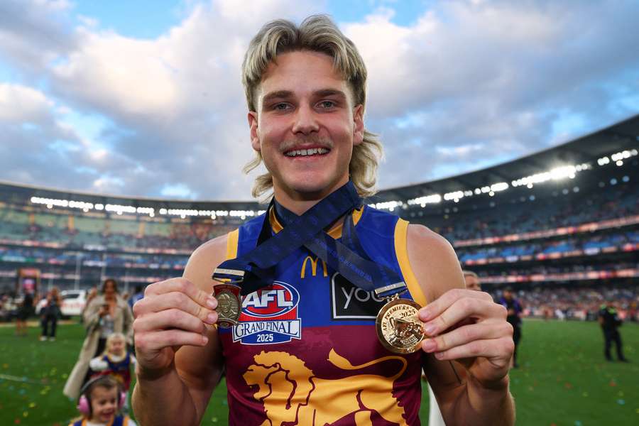 Will Ashcroft poses with his 2025 Norm Smith and Premiership medals.