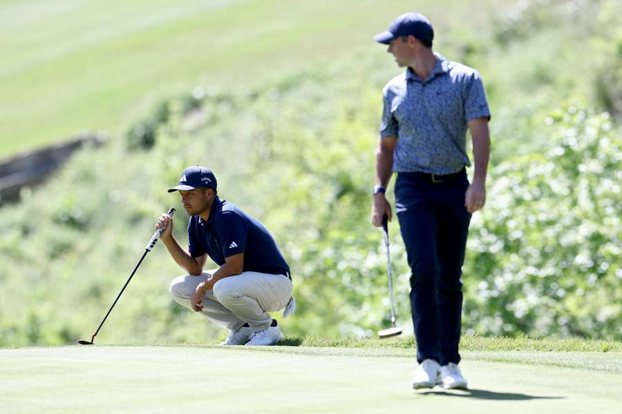 Xander Schauffele of the United States and Rory McIlroy of Northern Ireland line up putts on the ninth green 