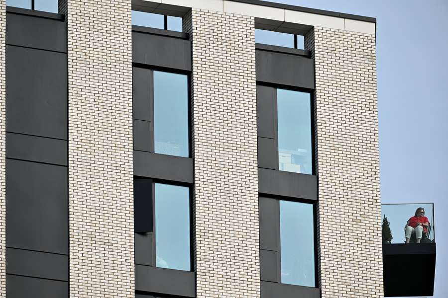 A resident sits on her balcony to watch the English Premier League football match between Brentford and Manchester City