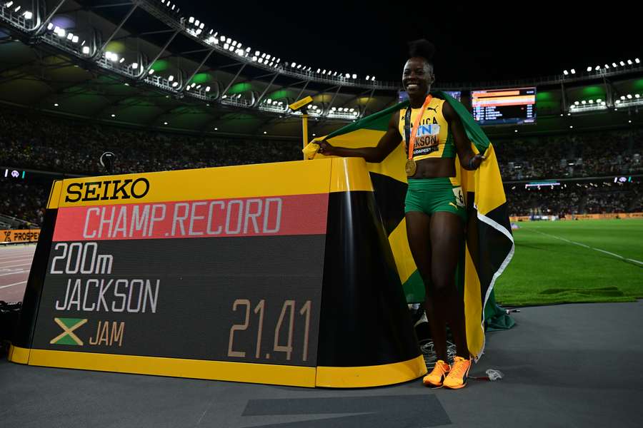 Shericka Jackson, medalha de ouro da Jamaica, festeja com a bandeira nacional e a medalha ao lado de um relógio que mostra o novo recorde do campeonato após a final dos 200 metros femininos