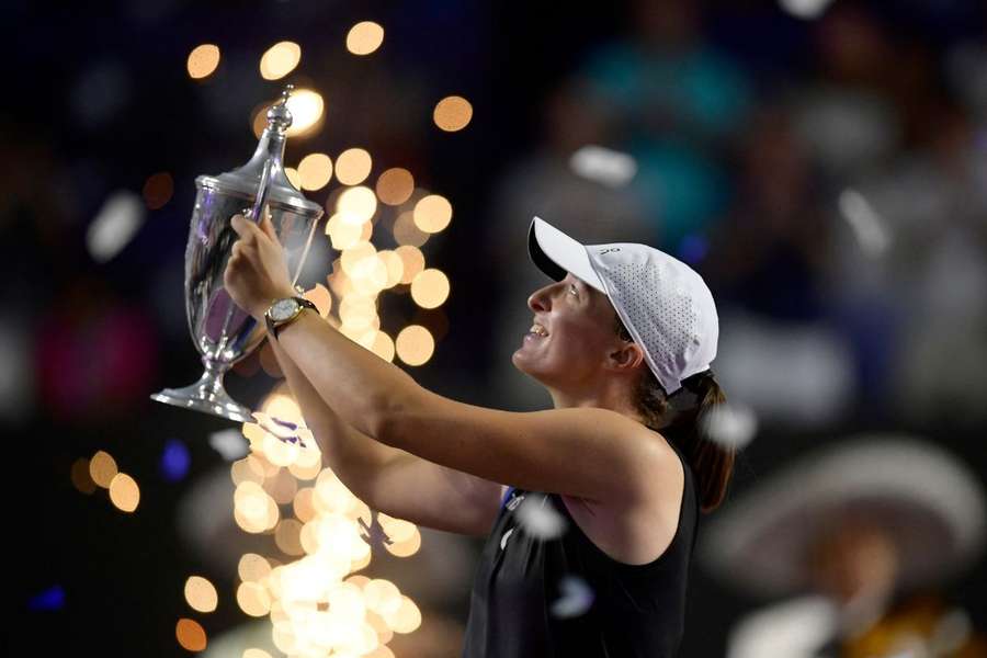 Iga Świątek wznosząca w górę trofeum za wygranie WTA Finals