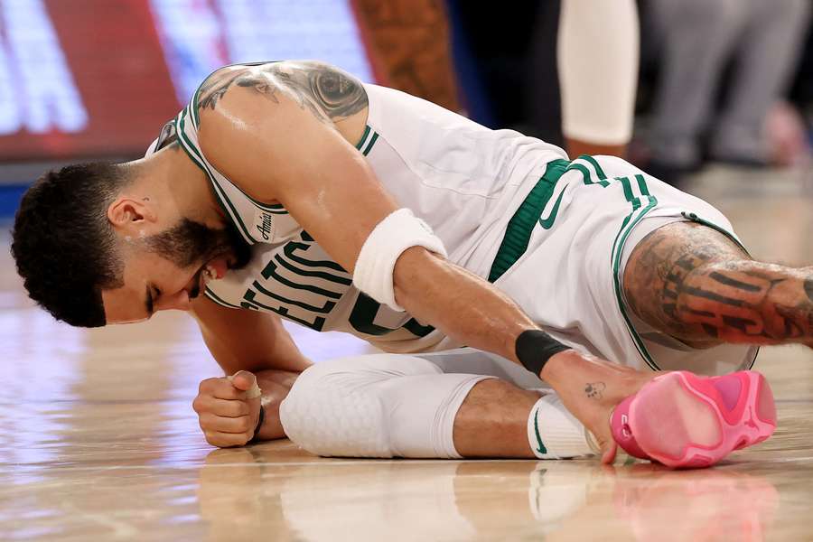 Tatum leva a mão no tornozelo direito 