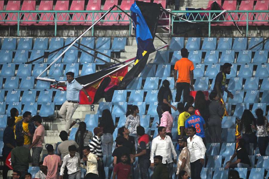 Spectators stand next to a billboard that fell due to strong winds