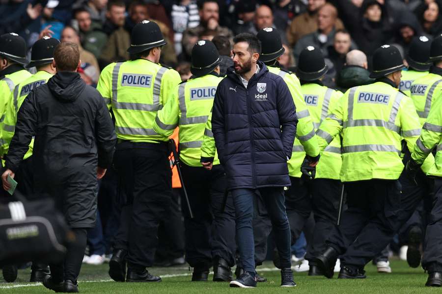West Bromwich Albion's Spanish head coach Carlos Corberan (C) walks away as police officers reinforce colleagues at the other end of the ground